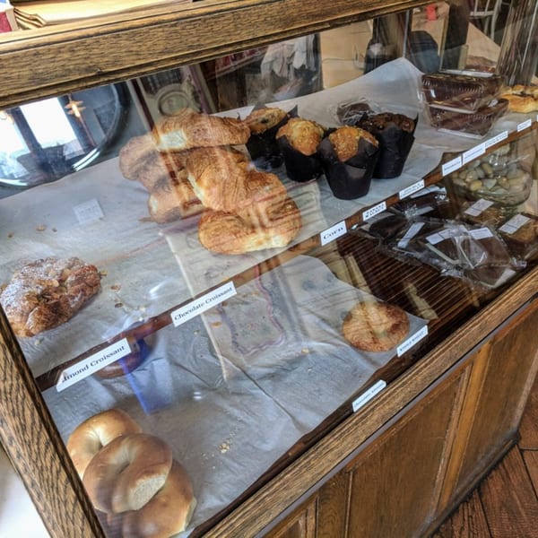 A glass display case at Roast & Co. filled with various pastries like croissants, muffins, and bagels.