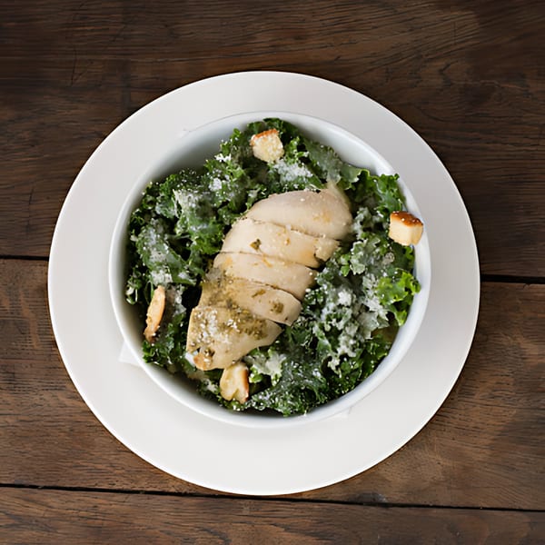 Overhead view of a Roast & Co. chicken Caesar salad with kale, croutons, and parmesan.