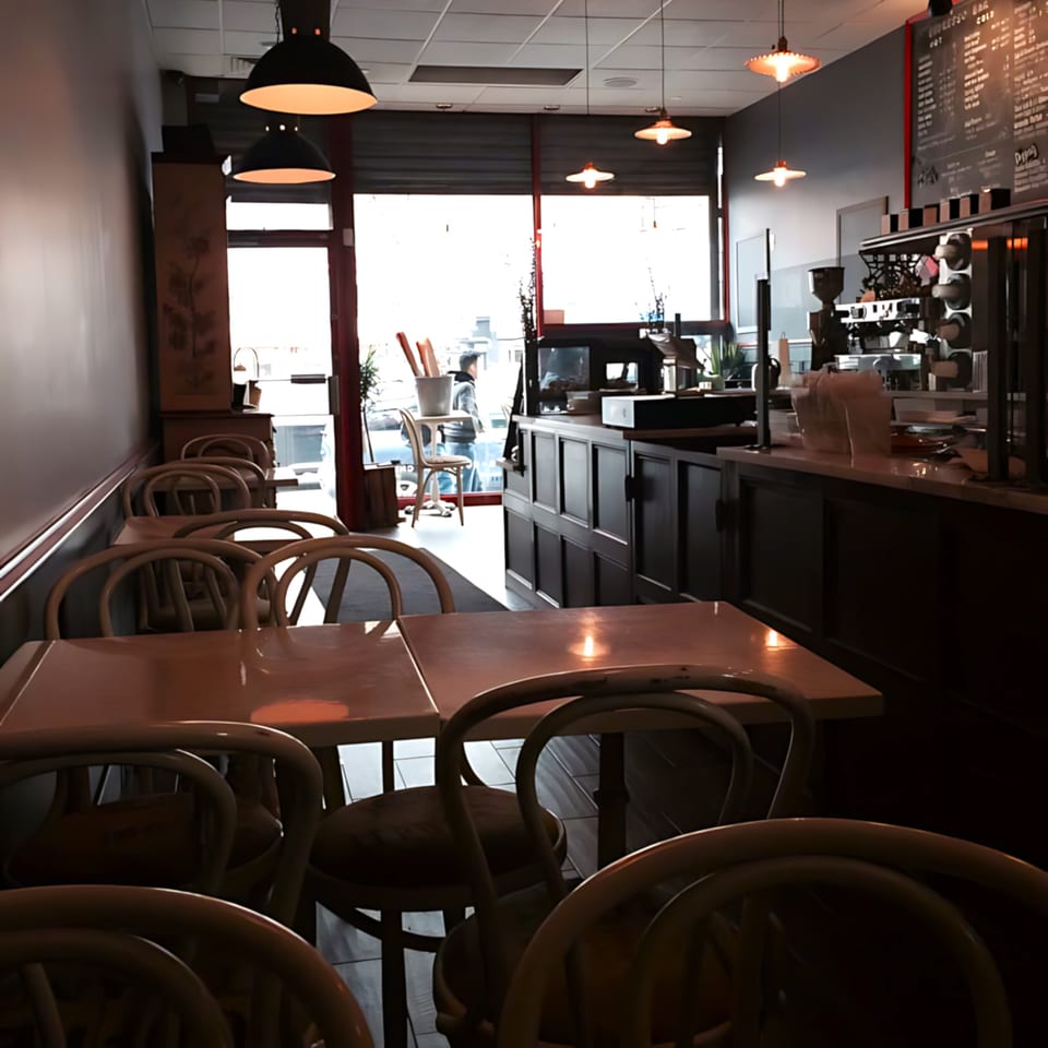Interior of Roast & Co. with empty tables and chairs, a counter with coffee machines, and bright windows.