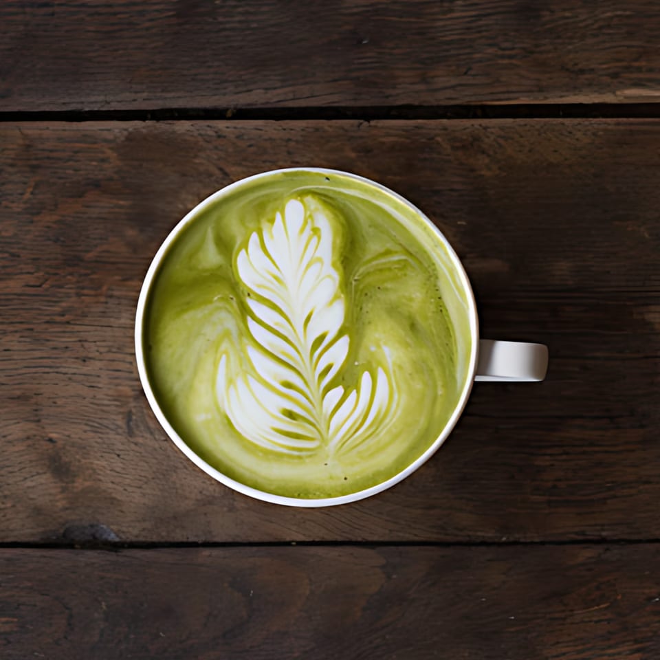 Overhead view of a green matcha latte with intricate white latte art on a dark wooden table.