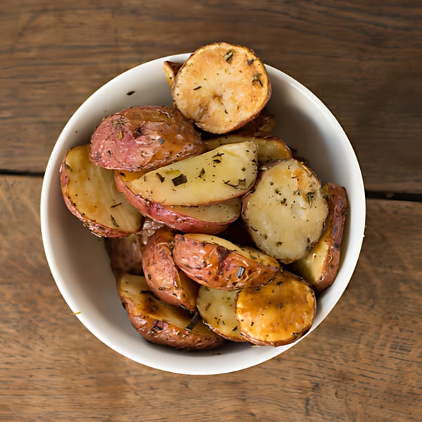 A white bowl filled with roasted red potatoes seasoned with herbs, on a wooden table.