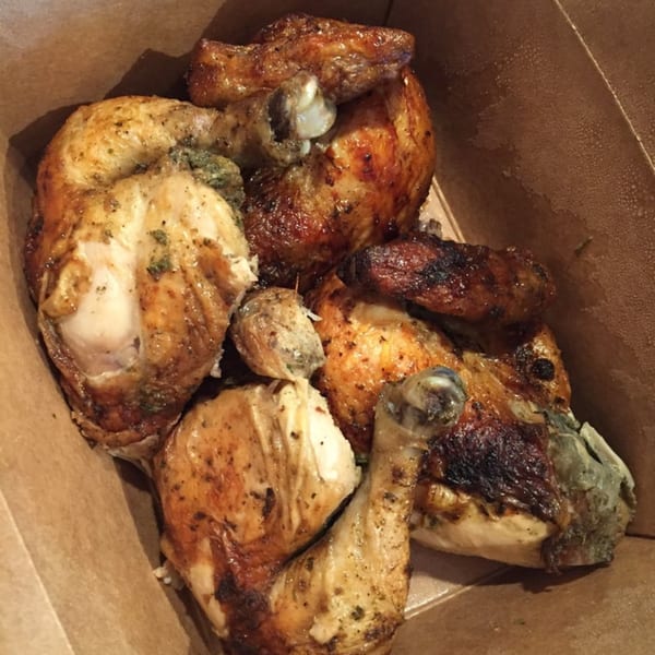 Several pieces of roasted chicken with crispy skin and herbs, served in a brown takeout box.